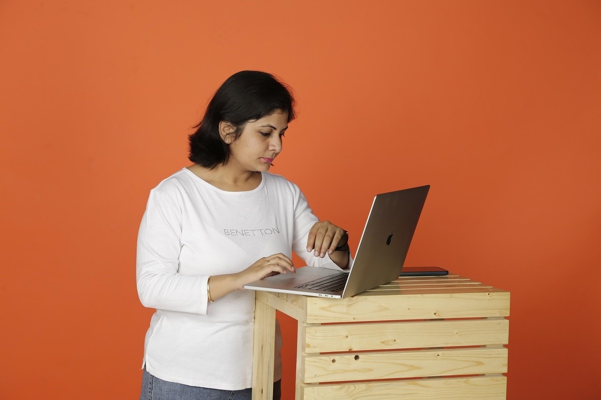 Une femme travaille sur son ordinateur portable devant un mur orange